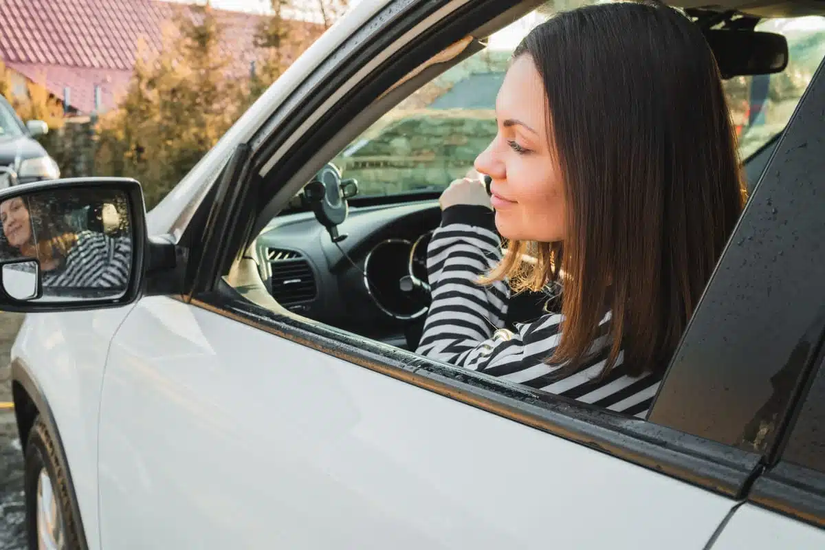 Woman leaning on the window of a white car, looking outside in a residential area.